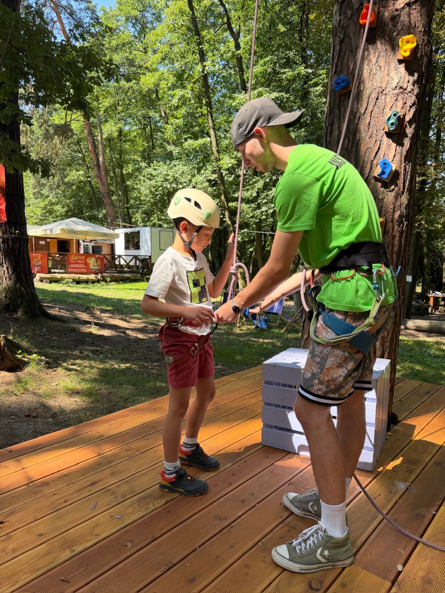 Instruktor zapina uprząż dziecku przed wejściem na ściankę wspinaczkową w Xtreme Park Wieliczka
